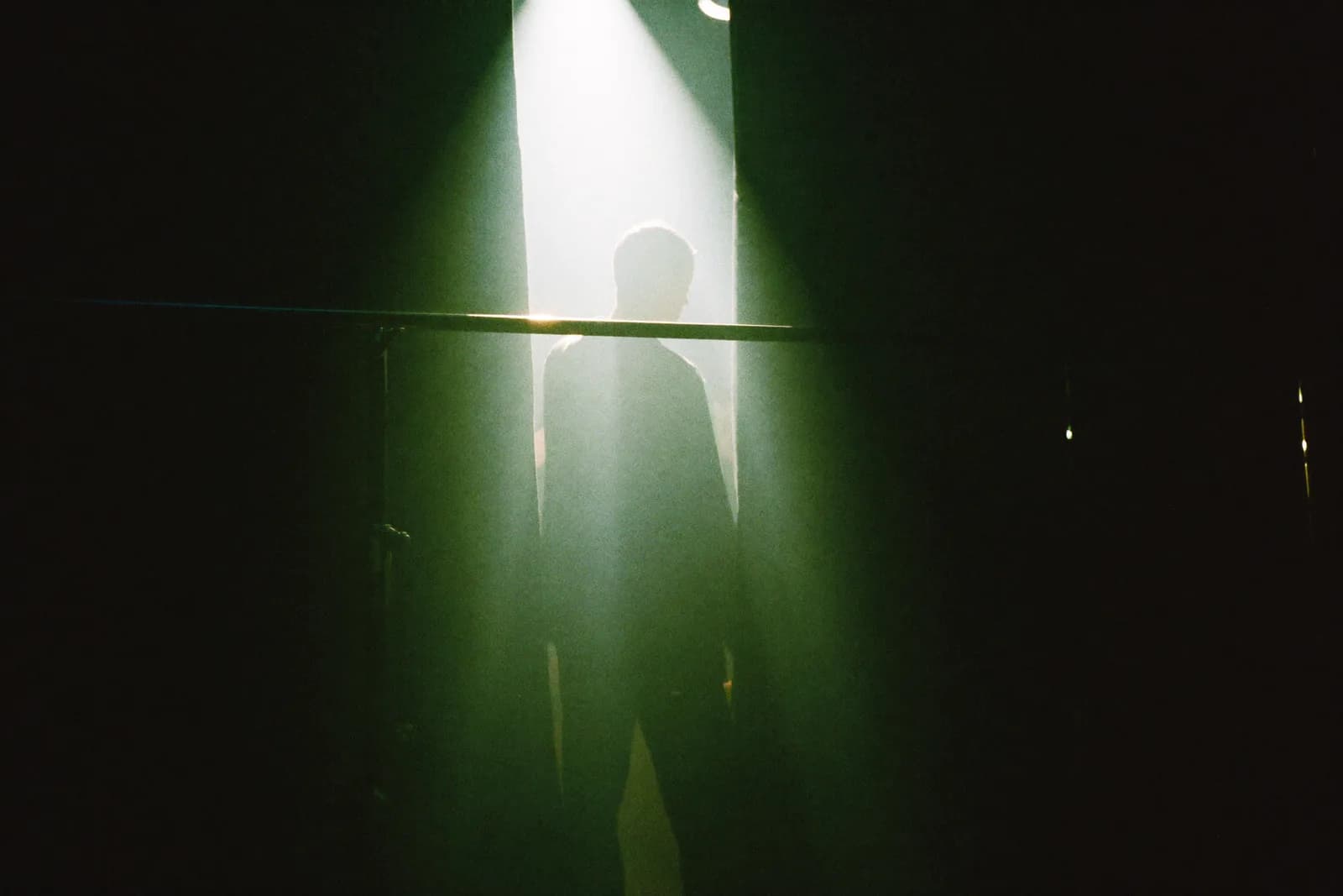 An artist silhouetted backstage, facing the stage lights through a gap in the curtain.